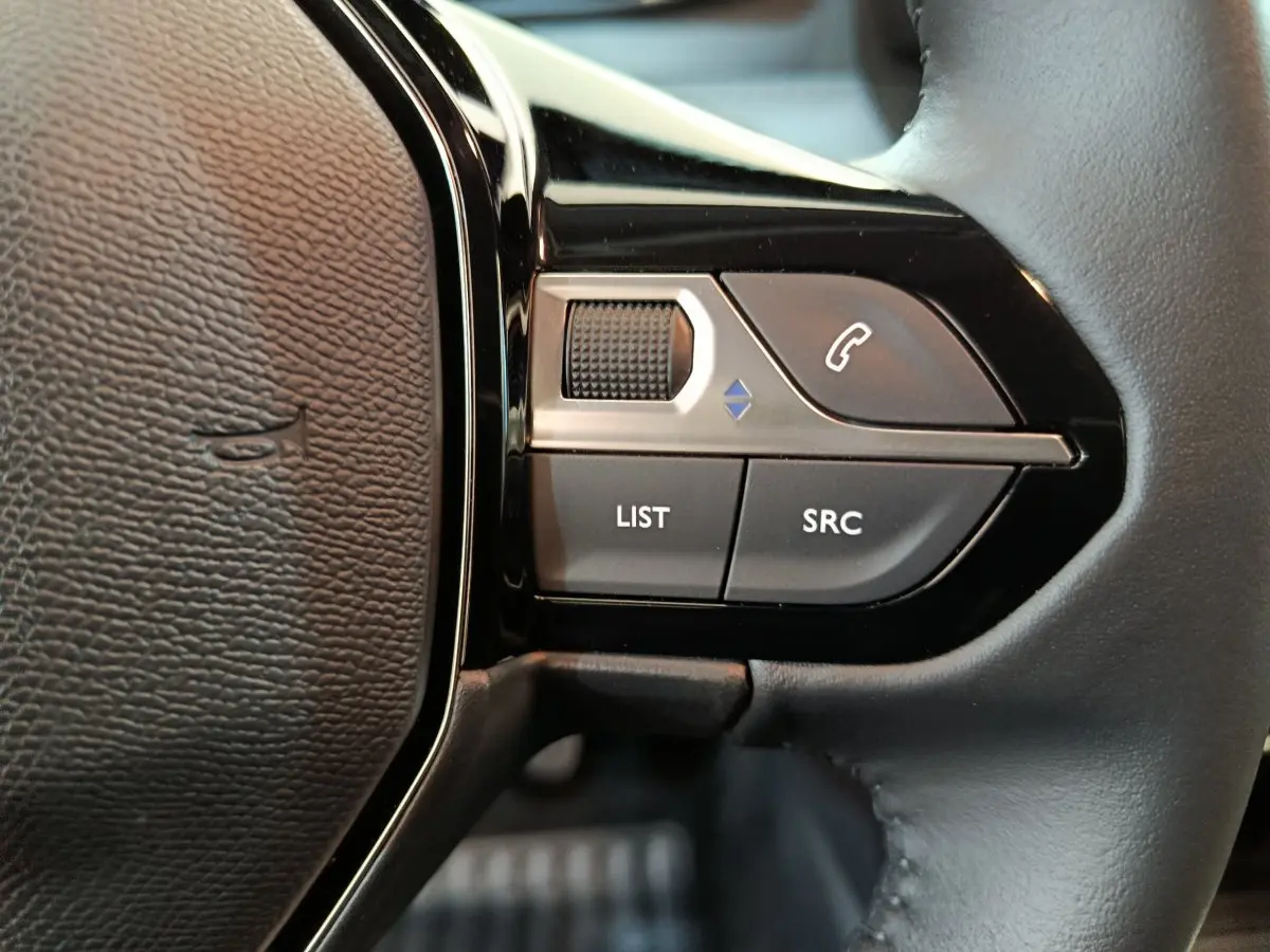 Gros plan sur les commandes gauche du volant cuir de la Peugeot 208 gris clair PureTech 100 S&S Allure 2025