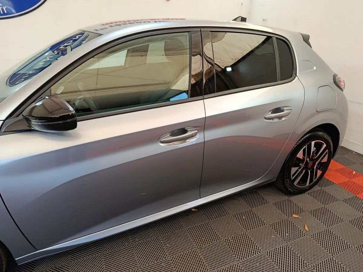 Profil côté gauche d'une Peugeot 208 gris clair 2025 avec rétroviseur noir et jantes alliage bicolores.