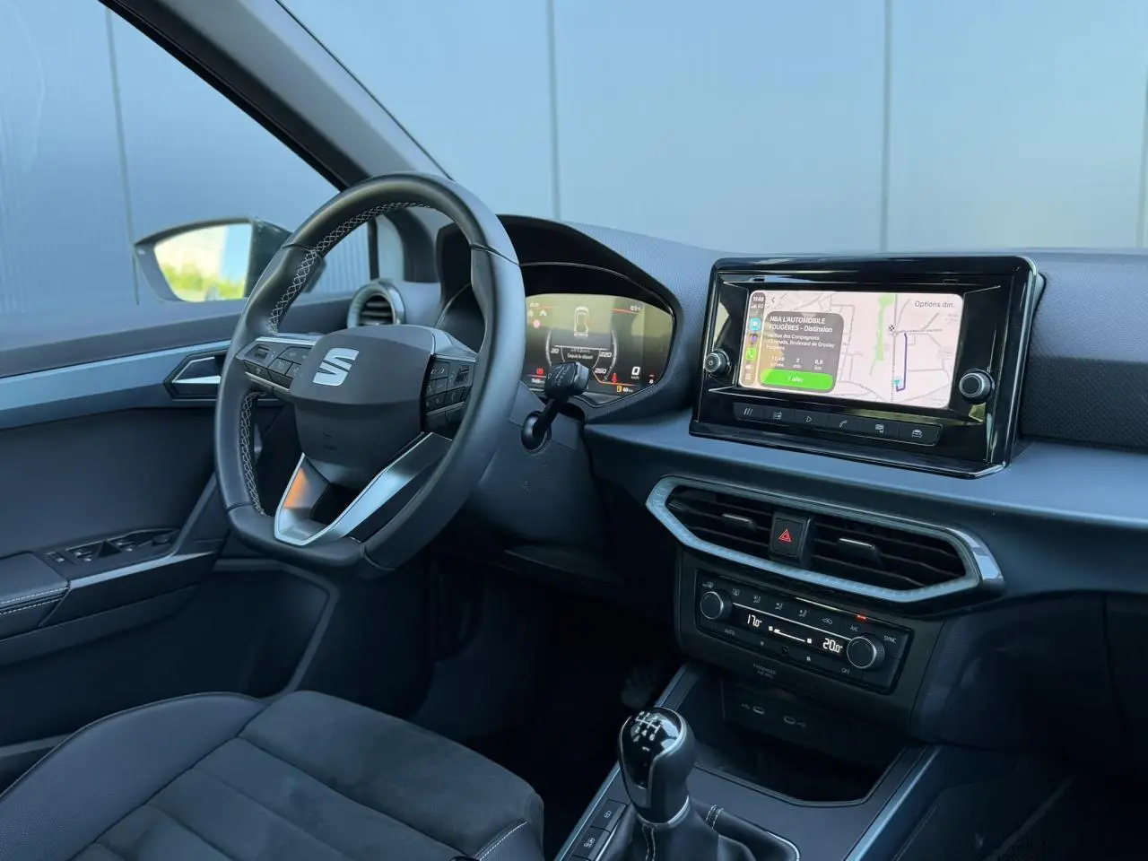 Vue intérieure côté conducteur du SEAT Arona TSI 115 Xpérience 2025, avec volant multifonction, écran tactile et levier de vitesse manuel.