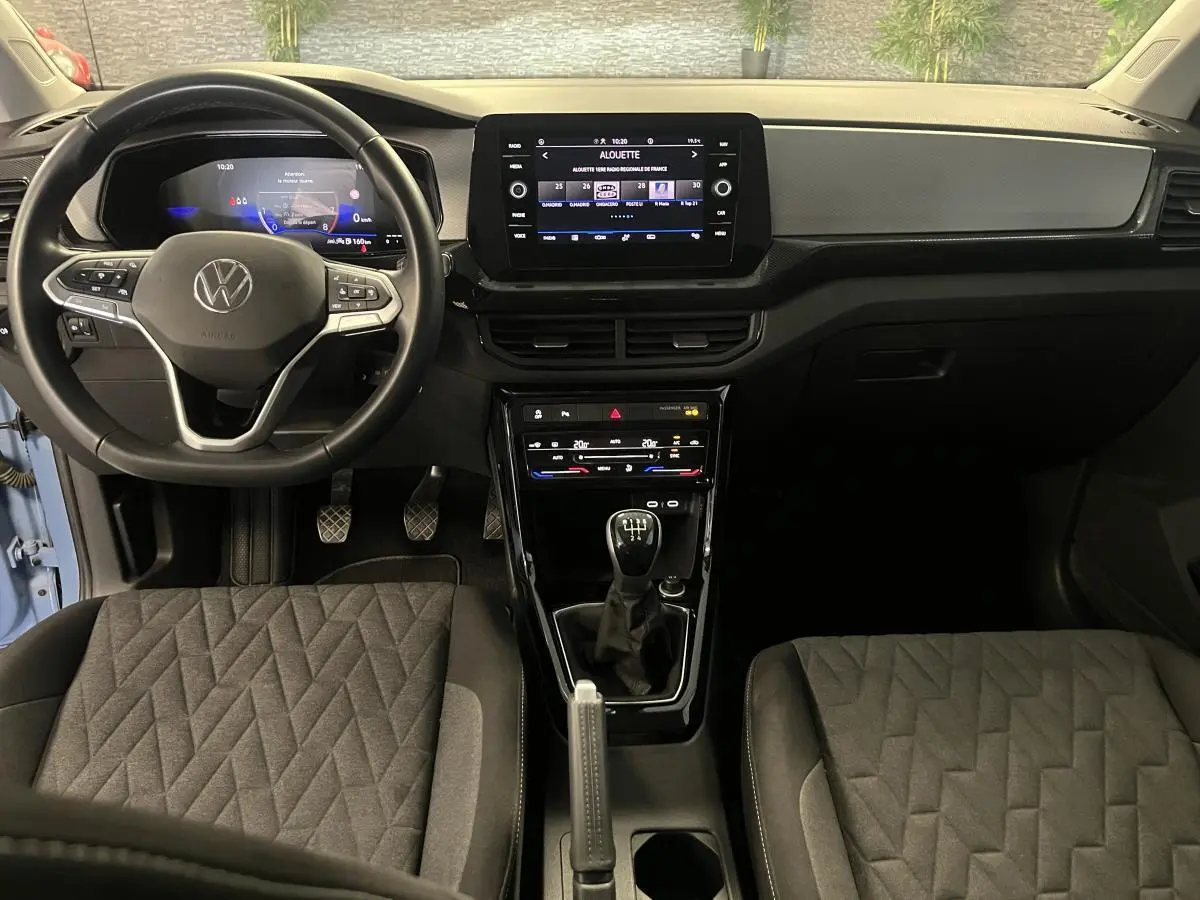 Intérieur du Volkswagen T-Cross 2024 bleu clair, vue frontale du tableau de bord avec volant cuir et levier manuel.