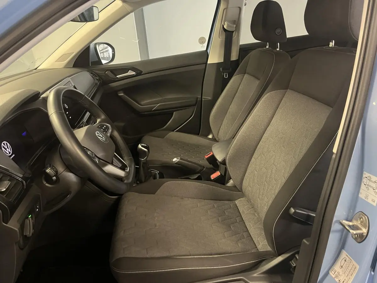 Intérieur avant du Volkswagen T-Cross bleu clair 2024, sièges tissu gris et volant multifonction en cuir visible côté conducteur.