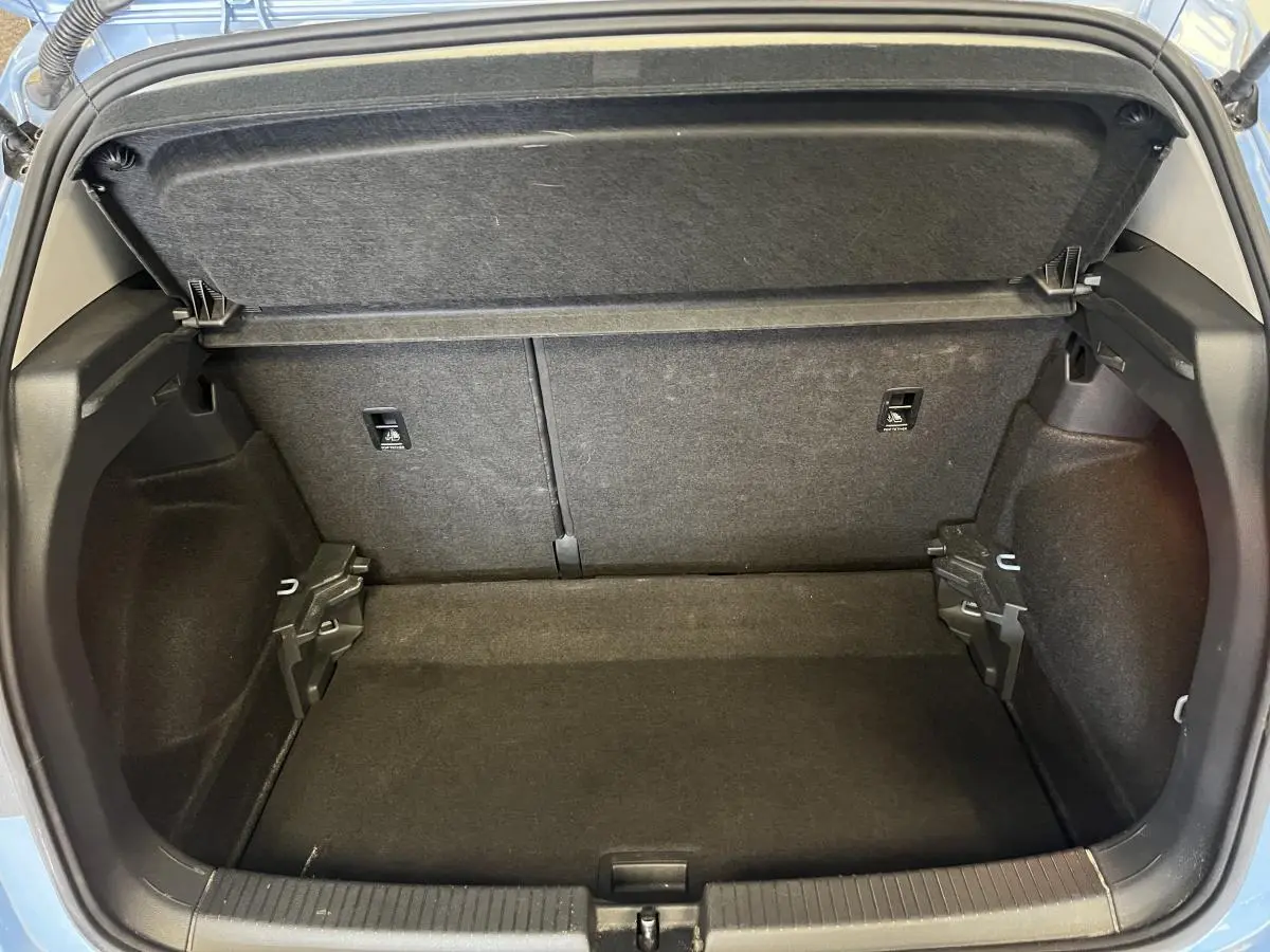Coffre ouvert du Volkswagen T-Cross bleu clair 2024, montrant l'espace de rangement intérieur vide et les finitions en tissu noir.