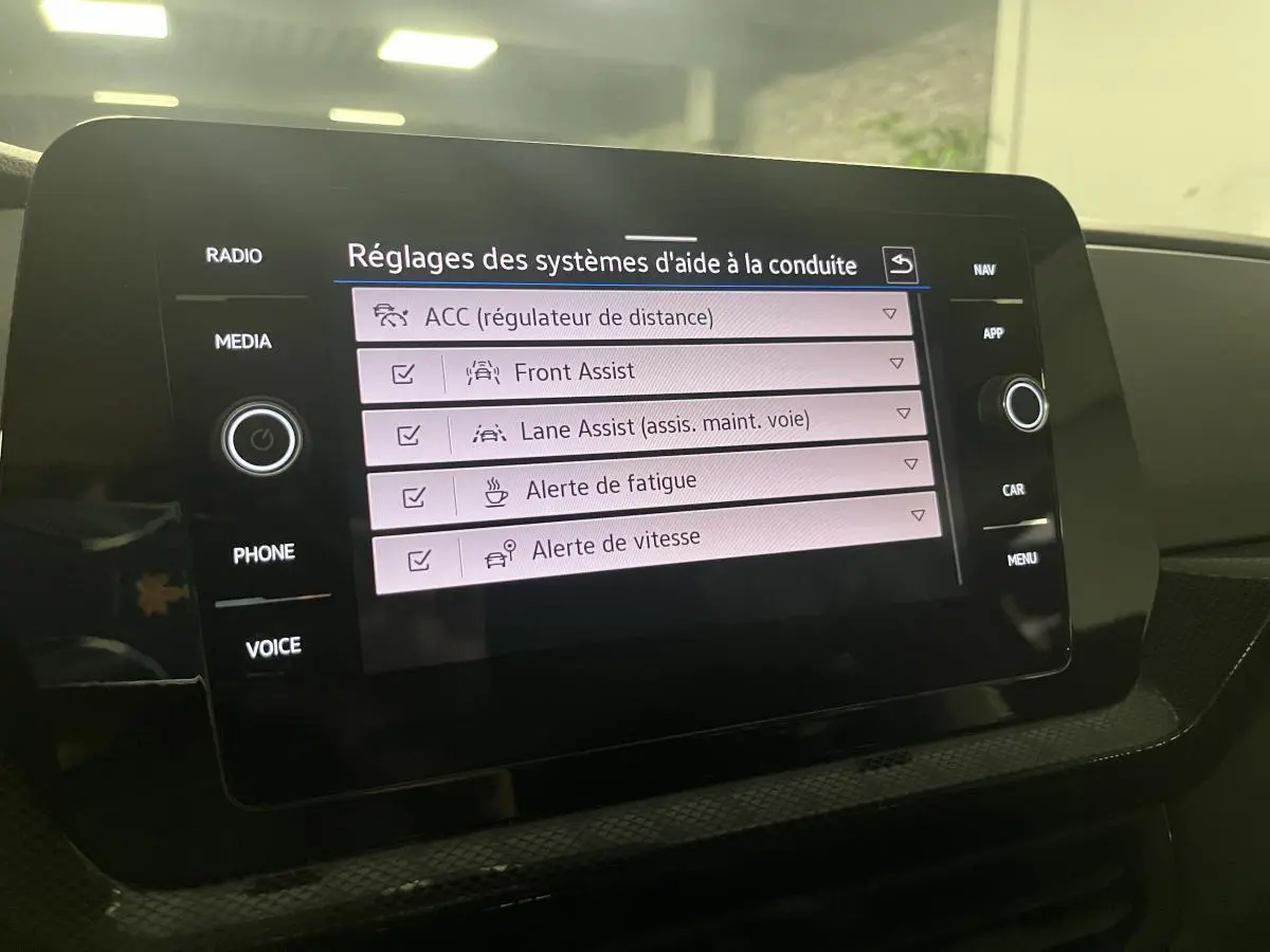 Écran tactile central du Volkswagen T-Cross 2024 affichant les réglages des aides à la conduite dans l'habitacle noir.