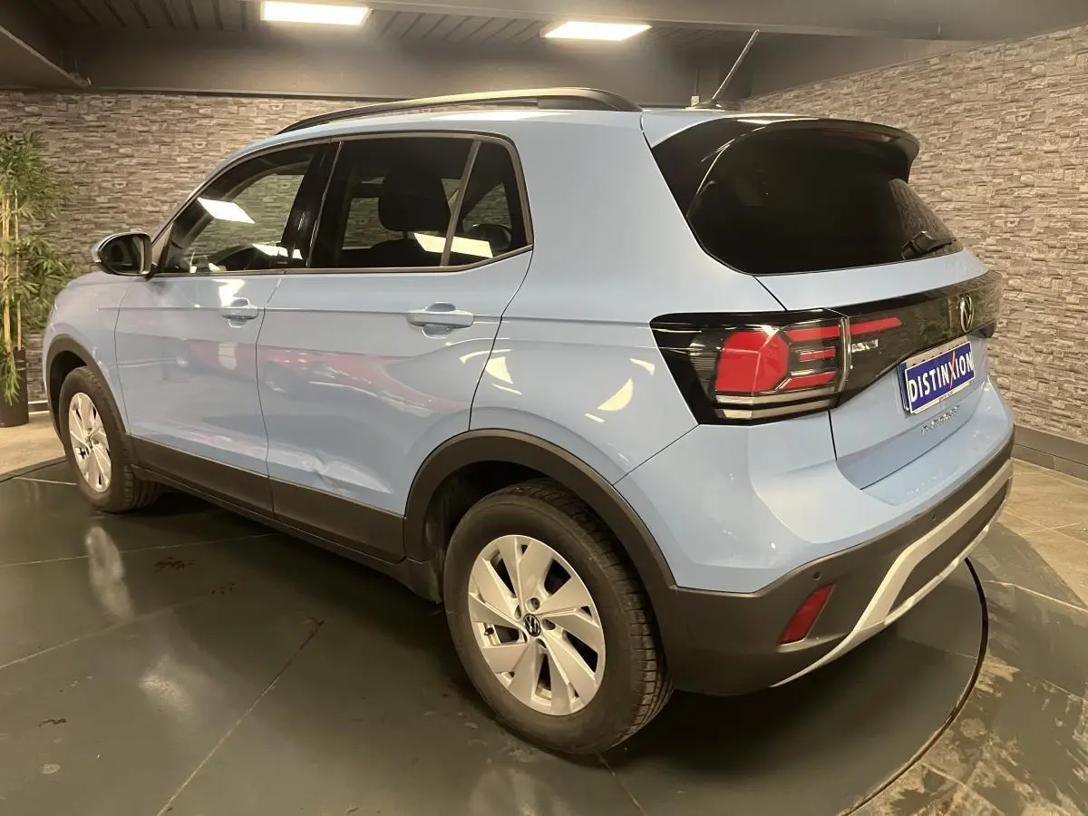 Vue 3/4 arrière droit d'un Volkswagen T-Cross bleu clair avec vitres arrière surteintées en intérieur showroom.