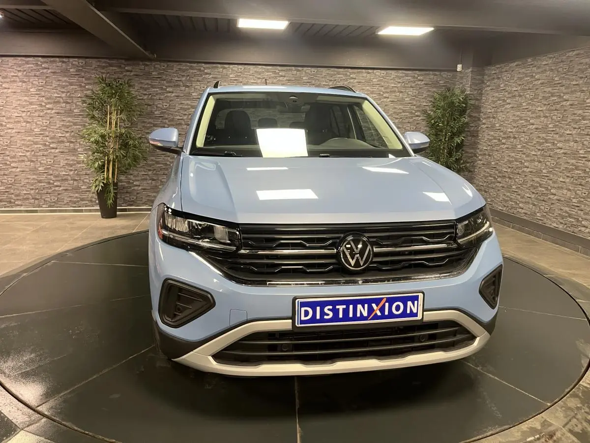 Volkswagen T-Cross bleu clair vue de face en intérieur, avec calandre noire et logo VW central bien visible.