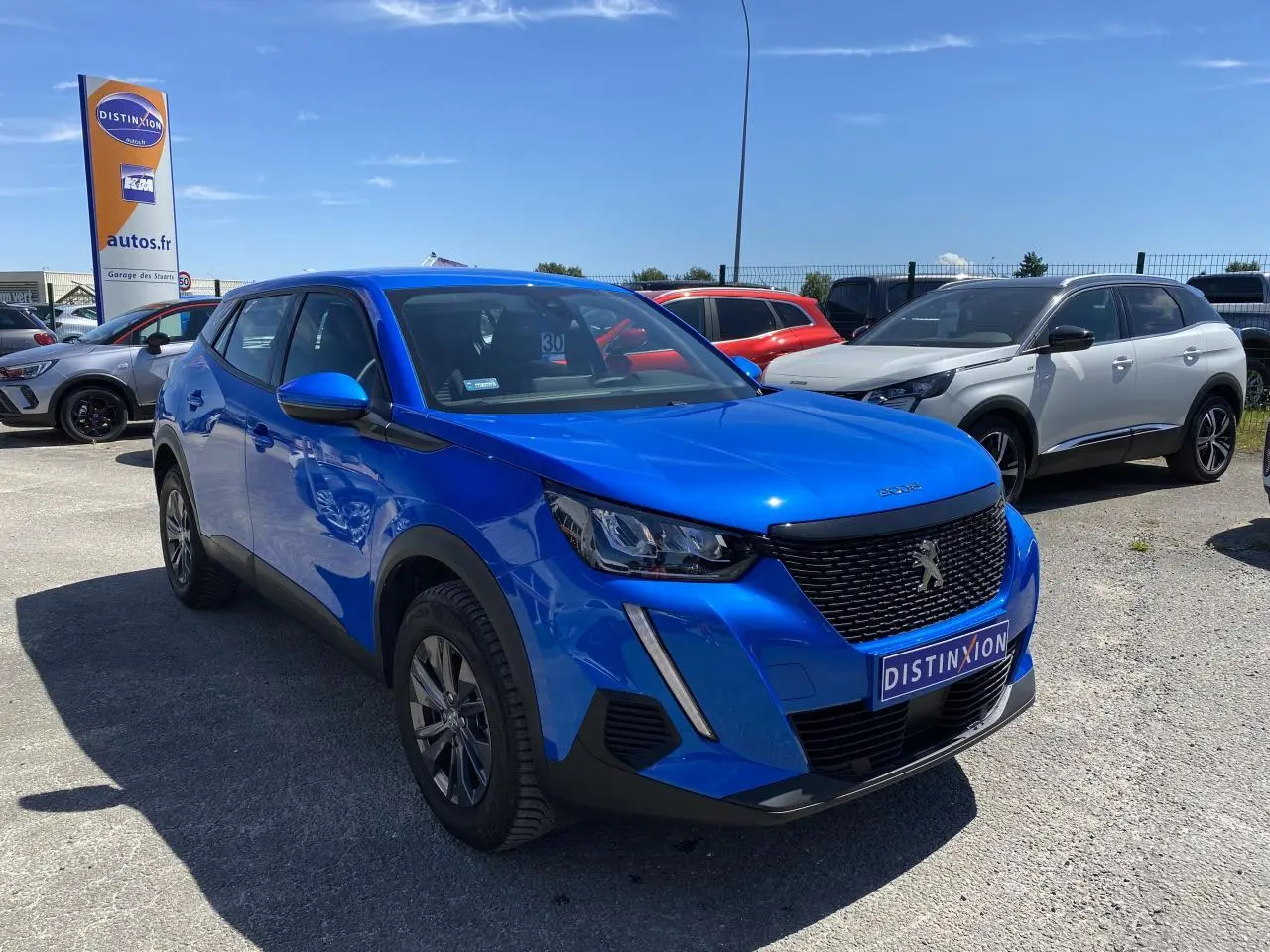 Peugeot 2008 bleu en 3/4 avant droit, avec calandre noire et feux LED, stationnée en extérieur au soleil.