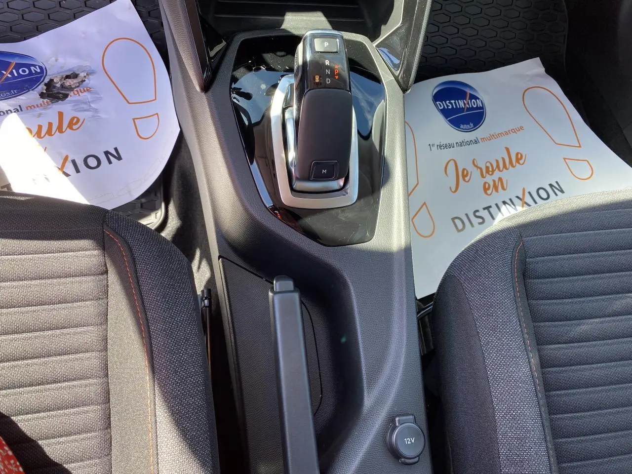 Vue plongeante sur la console centrale et levier de vitesse de la Peugeot 2008 bleu, avec sièges tissu gris et surpiqûres orange.