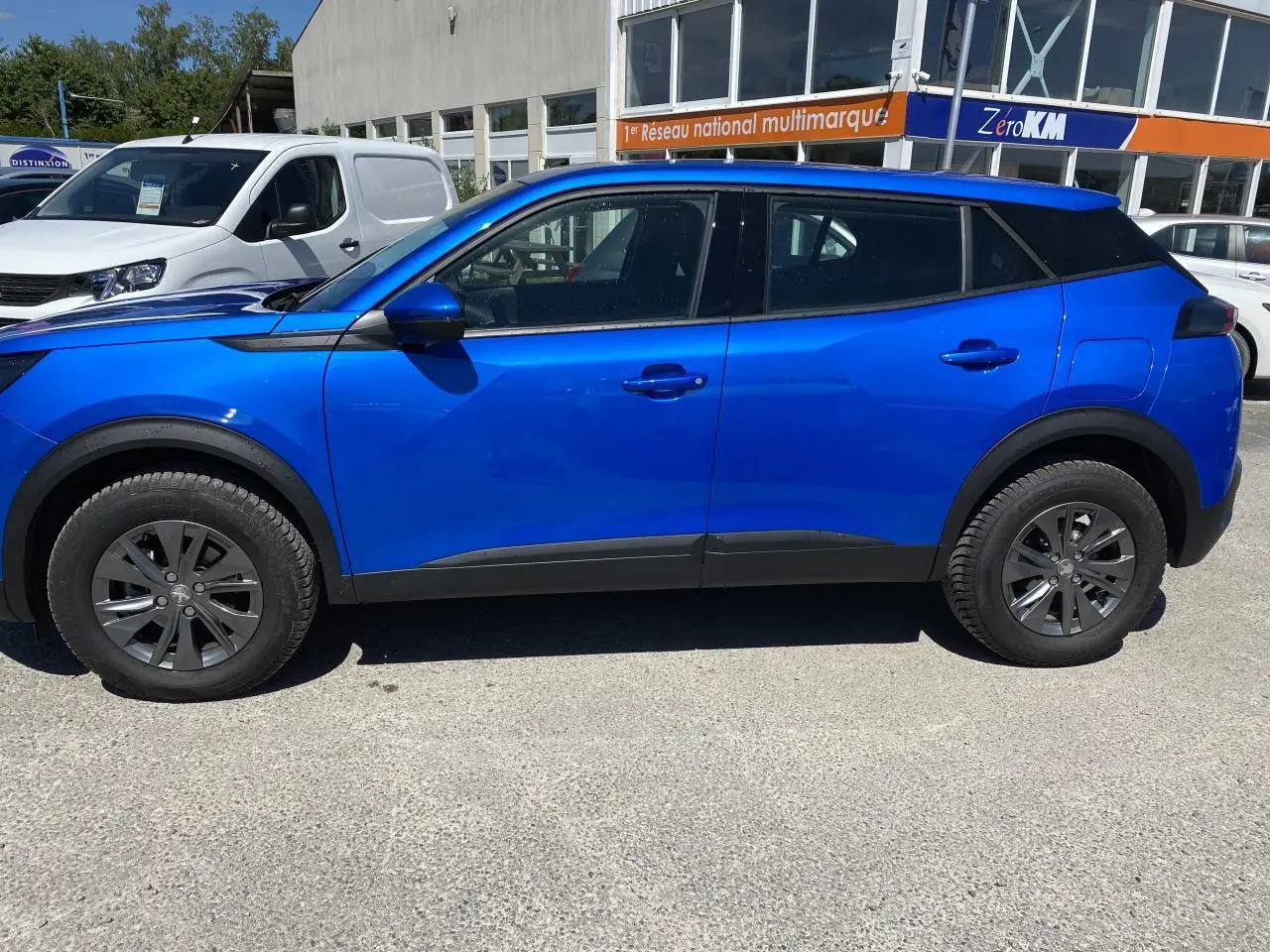 Profil côté gauche d'un Peugeot 2008 bleu 2021 Active Pack avec jantes foncées et protections noires sur les bas de caisse.