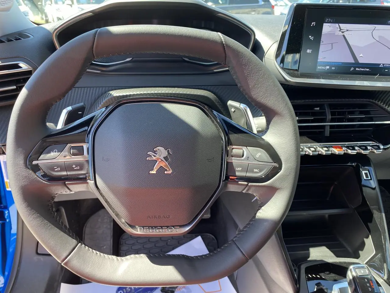 Vue rapprochée du volant cuir noir d'une Peugeot 2008 bleu 2021 avec tableau de bord et écran tactile visible.
