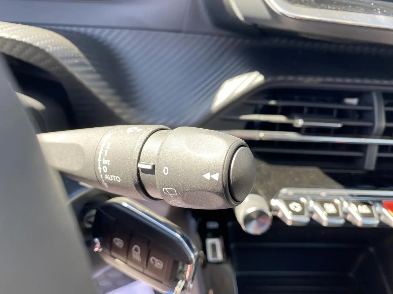 Gros plan sur la commande d'essuie-glace à gauche du volant dans l'habitacle noir d'un Peugeot 2008 bleu 2021.