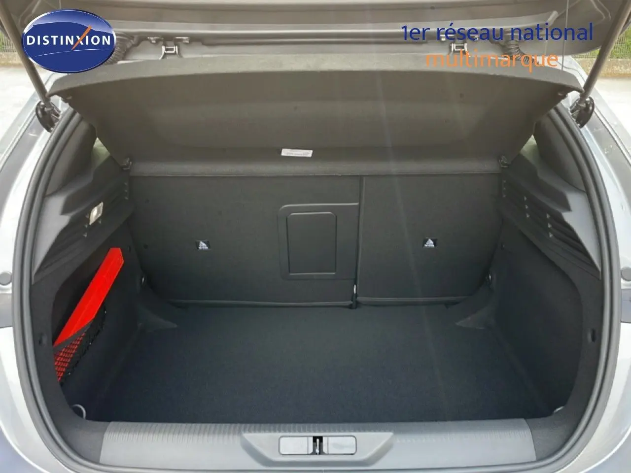 Coffre ouvert vu de l'arrière d'une Peugeot 308 gris Artense métal, avec rangement latéral et tapis noir.