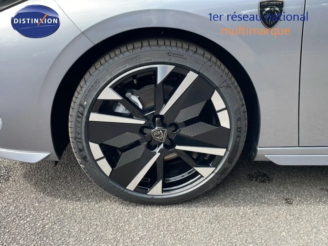 Gros plan sur la roue avant droite d’une Peugeot 308 gris Artense métal, jante alliage noire et argentée au design moderne.
