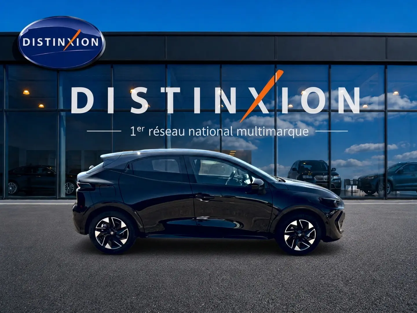 Profil latéral droit d'une Renault Clio VI noire 2026 avec jantes alliage et vitres teintées, devant une vitrine Distinxion.