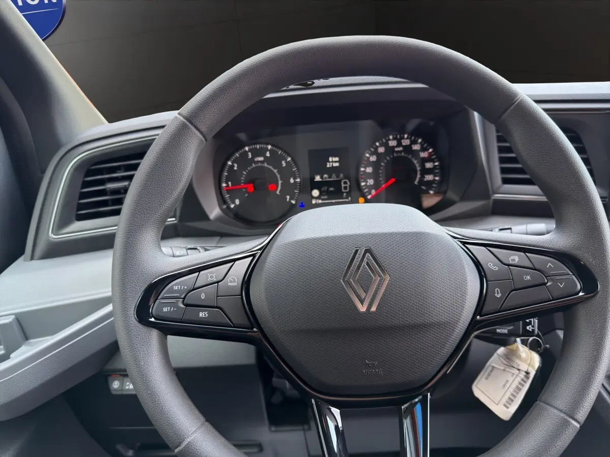 Vue rapprochée du volant gris du Renault Master 2026 avec commandes intégrées et tableau de bord numérique en arrière-plan.