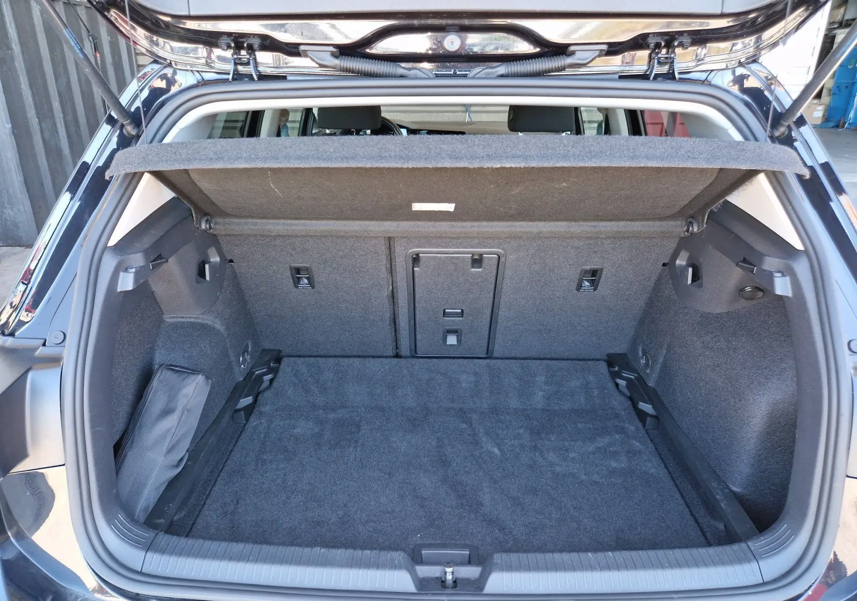 Coffre ouvert vu de l'arrière d'une Volkswagen Golf VIII noire métallisée, montrant l'espace de chargement et la tablette cache-bagages.