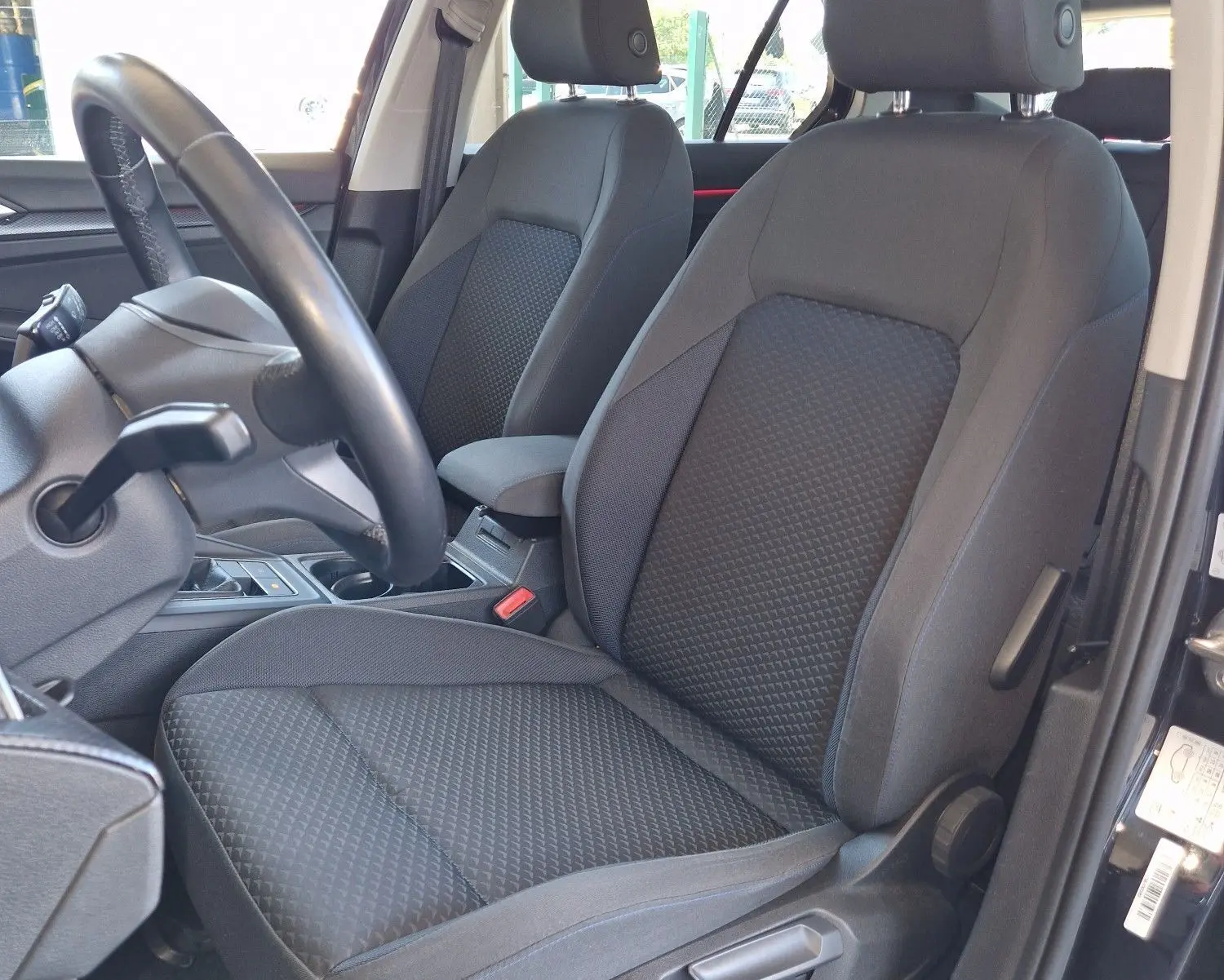 Vue intérieure côté conducteur de la Volkswagen Golf VIII noire, sièges tissu gris avec console centrale visible.