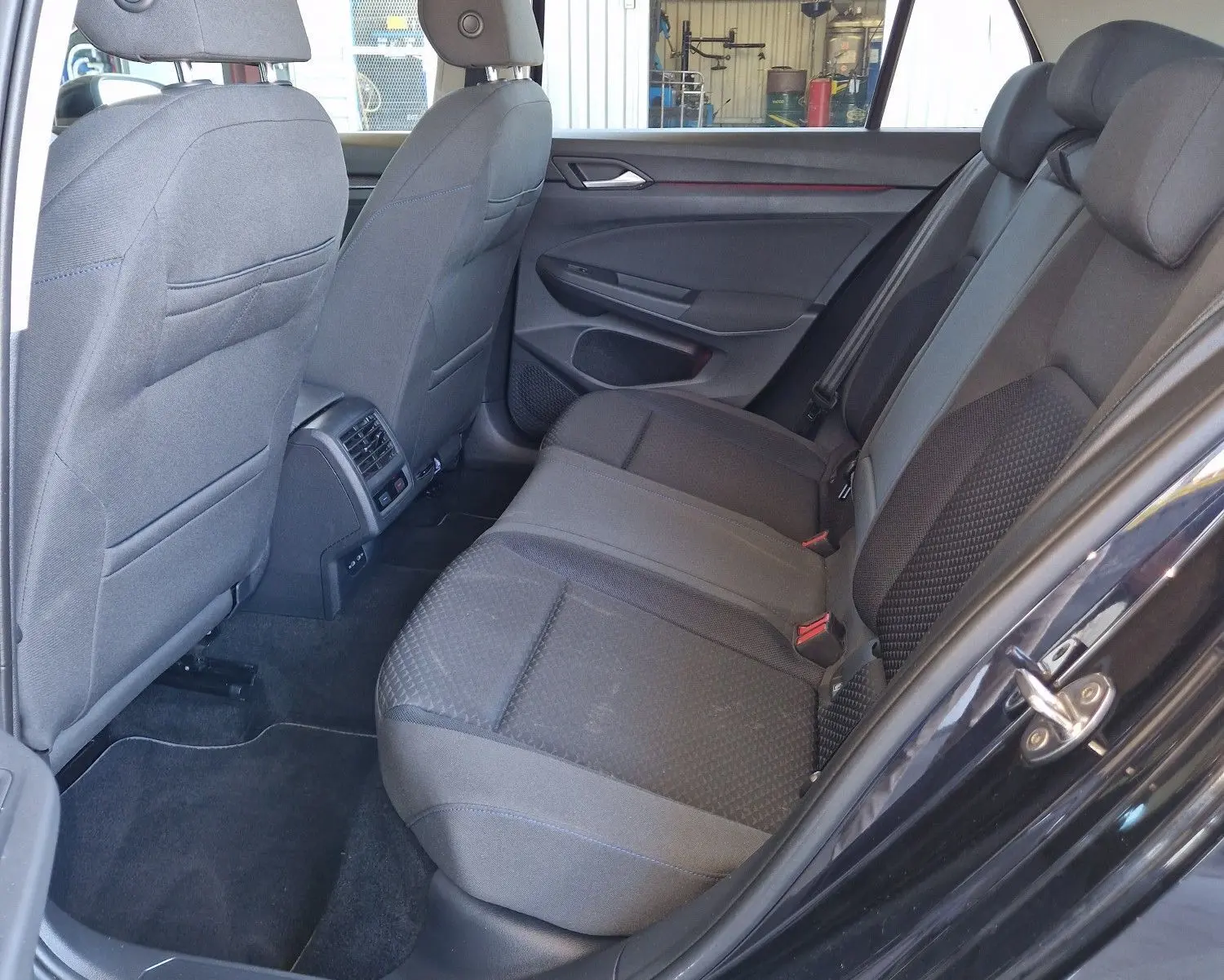 Intérieur arrière côté gauche d'une Volkswagen Golf VIII noire, sièges tissu gris et espace passagers visible.