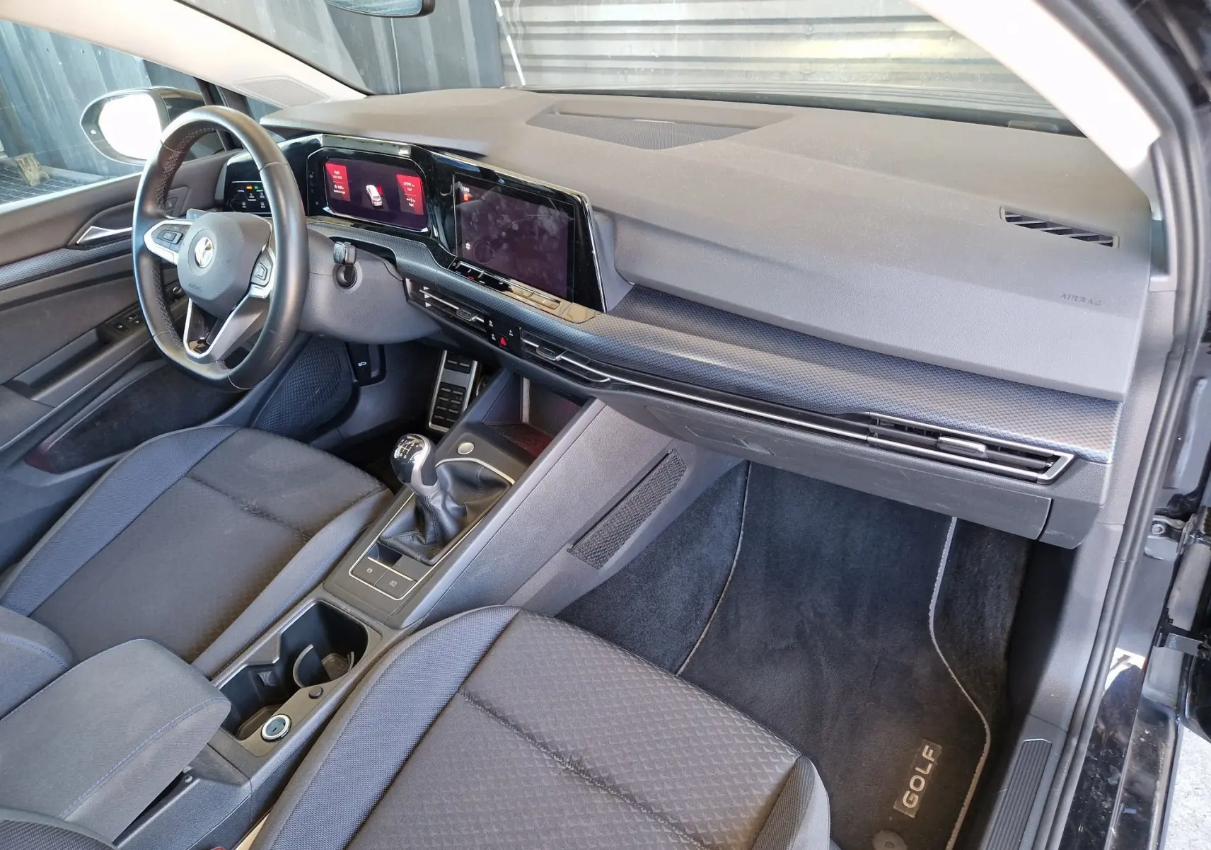 Intérieur côté conducteur de la Volkswagen Golf VIII noire, avec tableau de bord moderne et boîte manuelle visible.