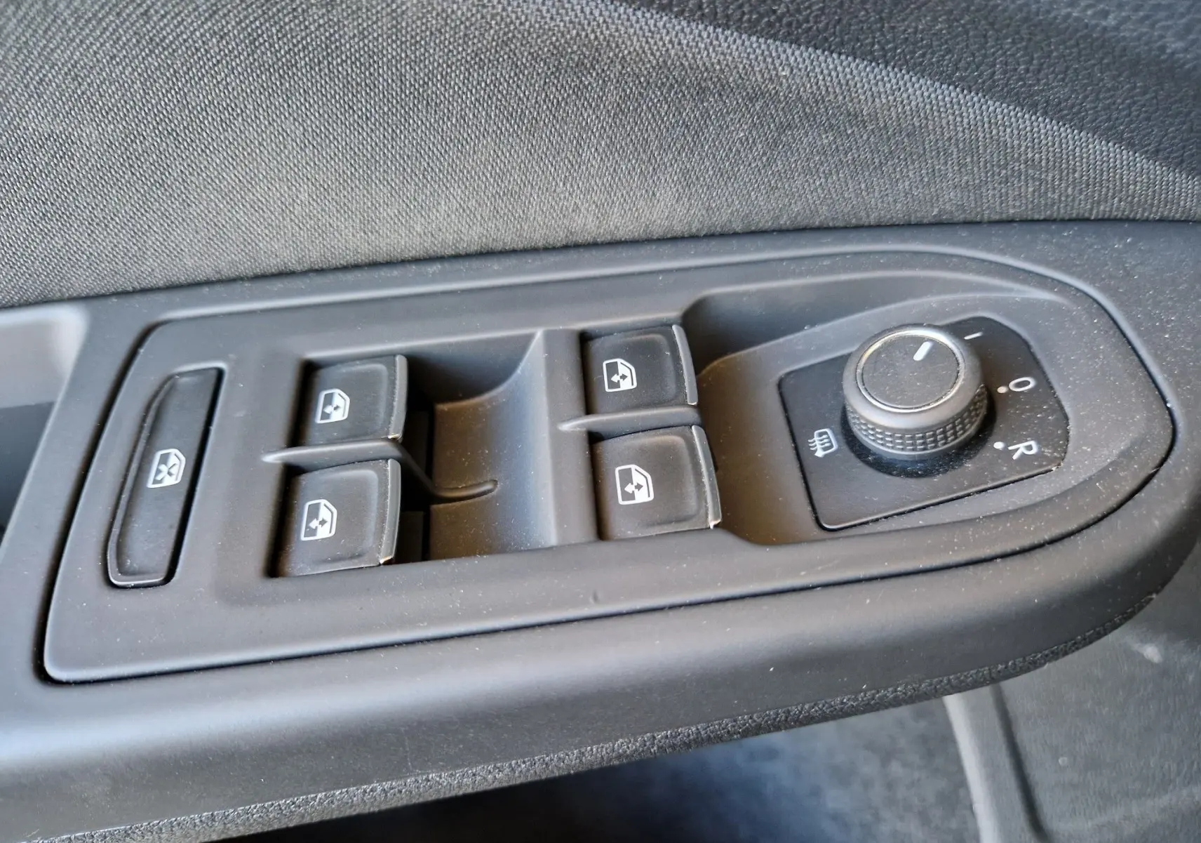 Gros plan sur les commandes de lève-vitres et réglage des rétroviseurs côté conducteur d'une Volkswagen Golf VIII noire.