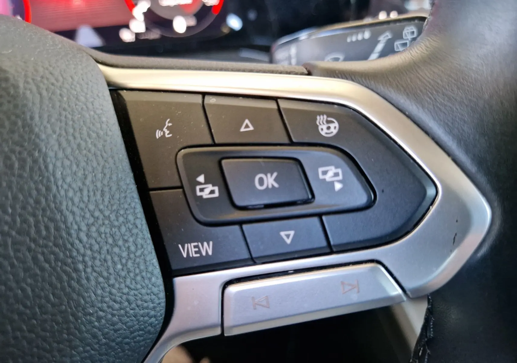 Gros plan sur les commandes multifonctions noires et argentées du volant d'une Volkswagen Golf VIII noire de 2021.