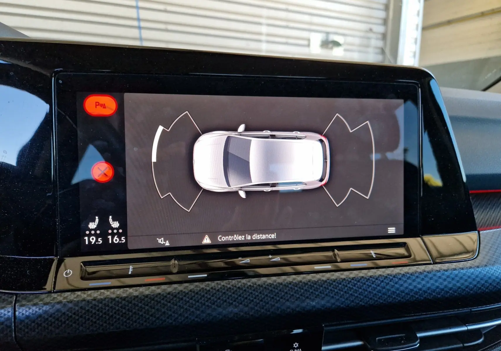 Écran central de la Volkswagen Golf VIII noir métal montrant l'alerte de distance avec commandes tactiles et climatisation.