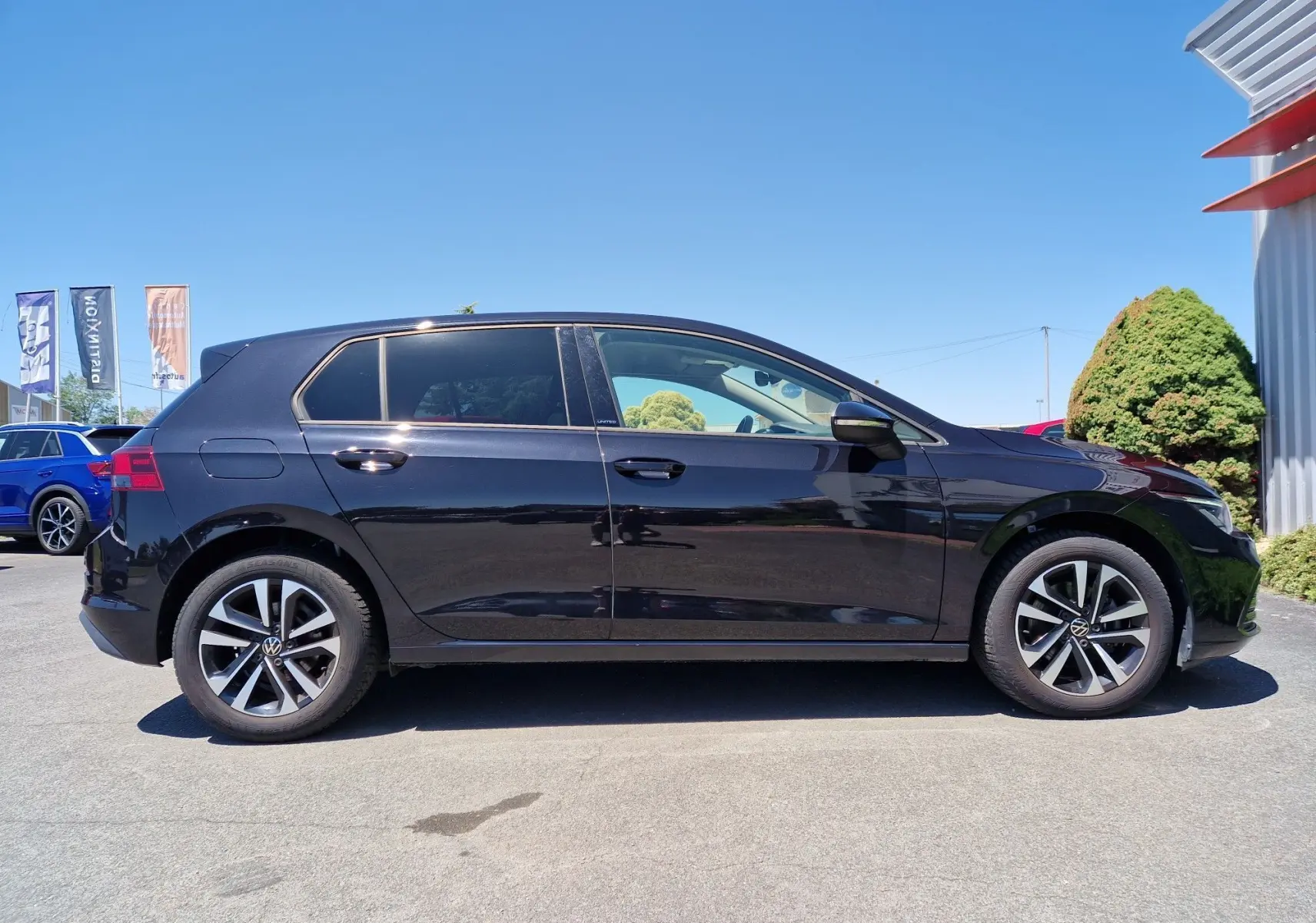 Profil latéral droit d'une Volkswagen Golf VIII noire métallisée, avec jantes alliage et cinq portes visibles.