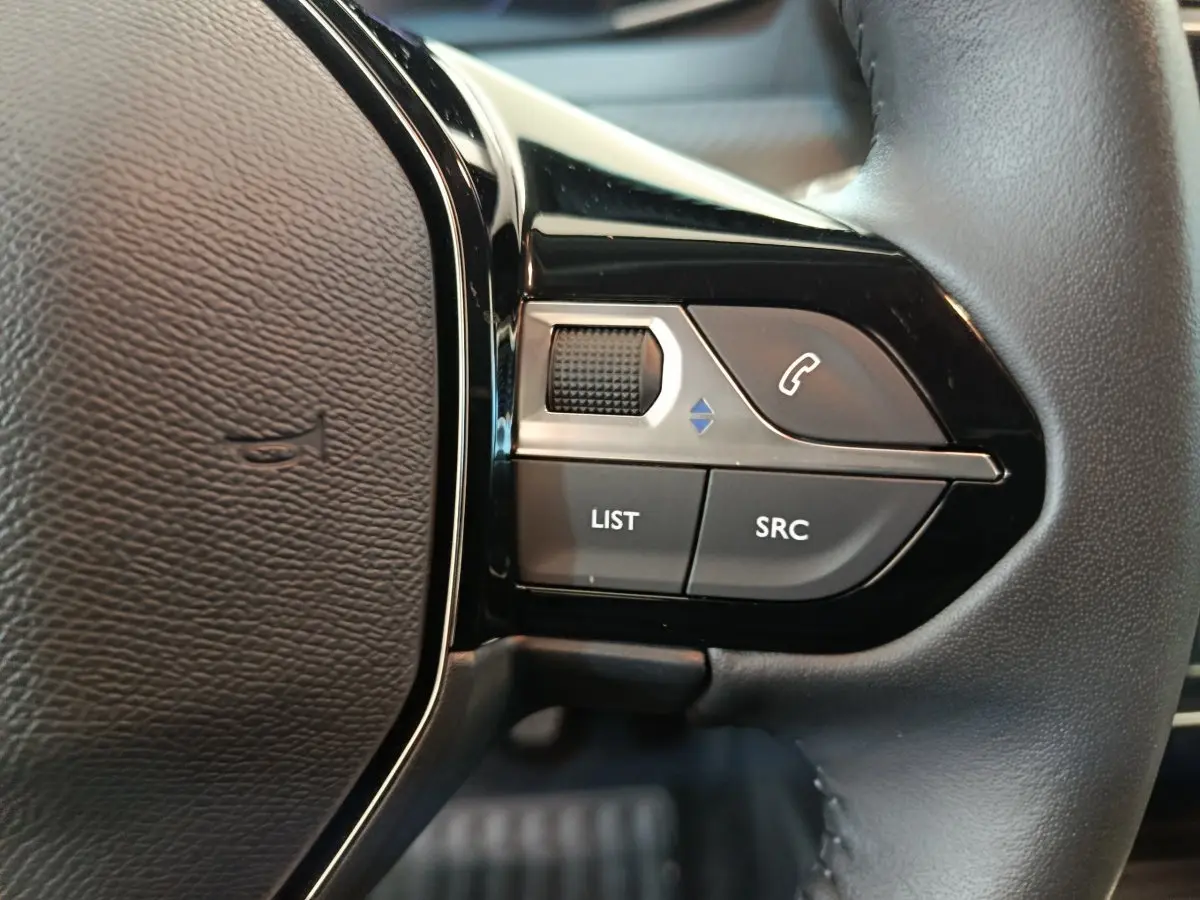 Gros plan sur les commandes gauche du volant cuir de la Peugeot 208 gris foncé, version PureTech 100 S&S Allure 2025.