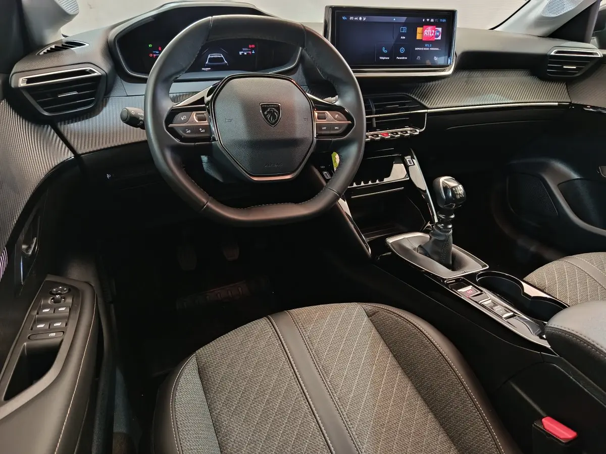 Intérieur avant de la Peugeot 208 PureTech 100 S&S Allure 2025, vue du conducteur sur le tableau de bord et volant cuir.