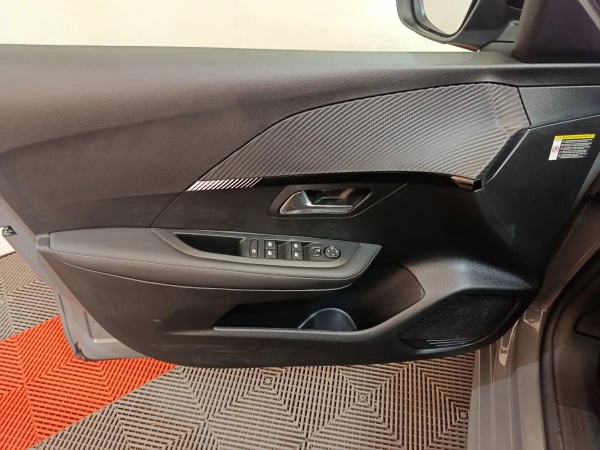 Vue côté gauche de la porte avant gris foncé du Peugeot 208 PureTech 100 S&S Allure avec commandes électriques et insert carbone.