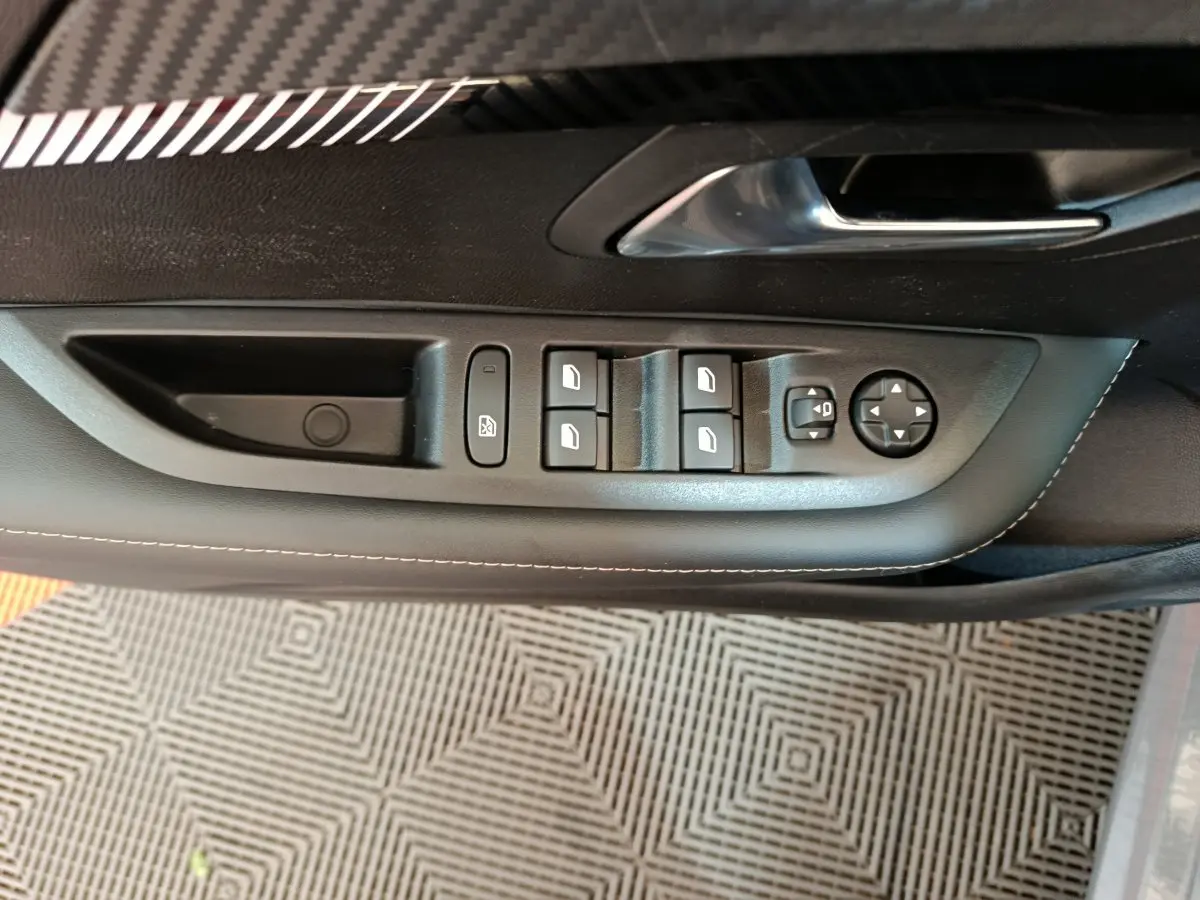 Panneau de commande des vitres et rétroviseurs côté conducteur de la Peugeot 208 gris foncé, vue intérieure rapprochée.