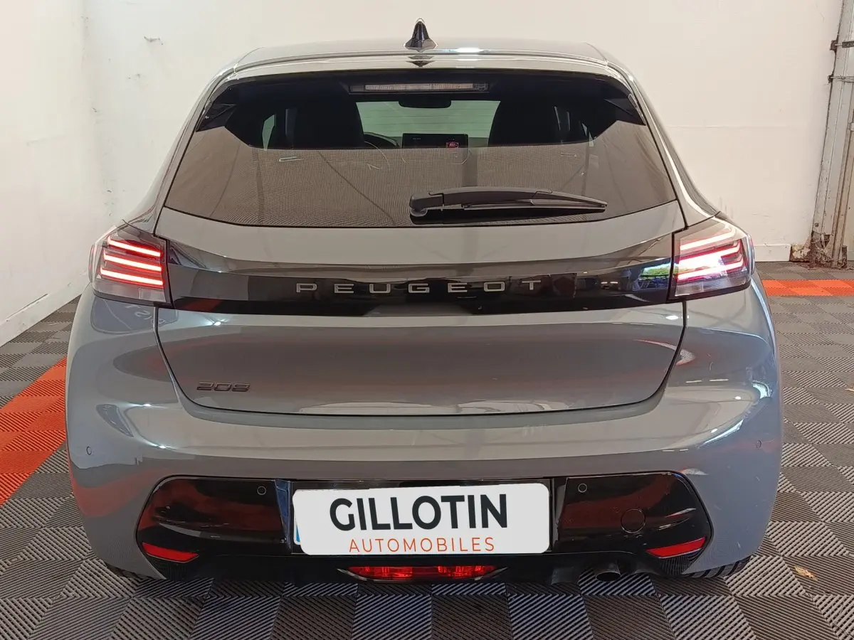 Vue arrière d'une Peugeot 208 gris foncé avec feux LED allumés et logo Peugeot visible sur le hayon.