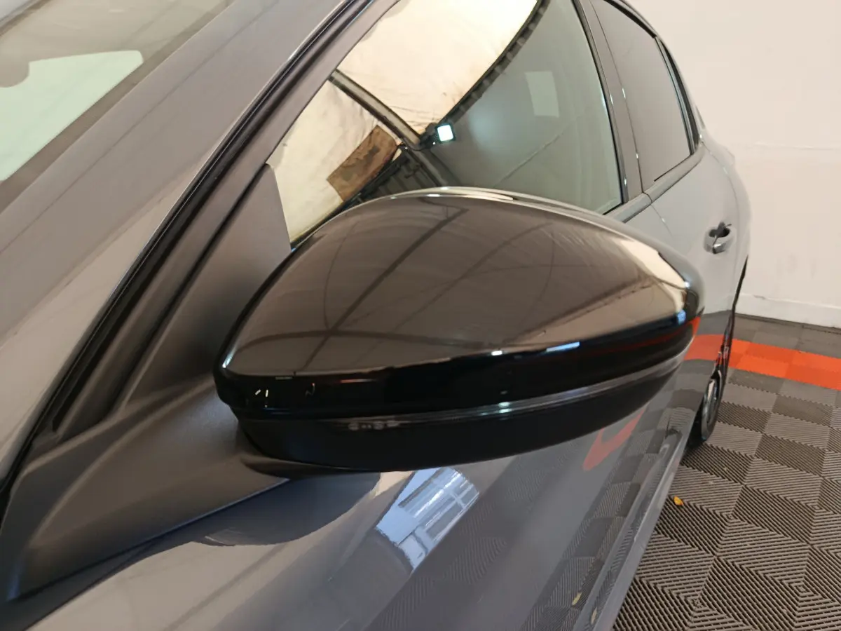 Rétroviseur noir brillant côté gauche d'une Peugeot 208 gris foncé vue en gros plan sur fond intérieur.