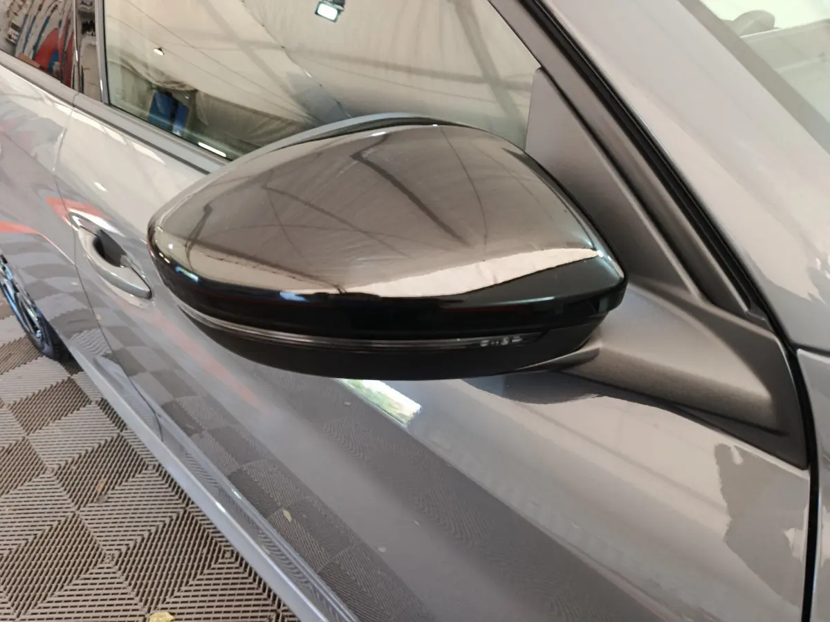 Rétroviseur noir côté gauche d'une Peugeot 208 gris foncé, vue rapprochée sur la portière avant.