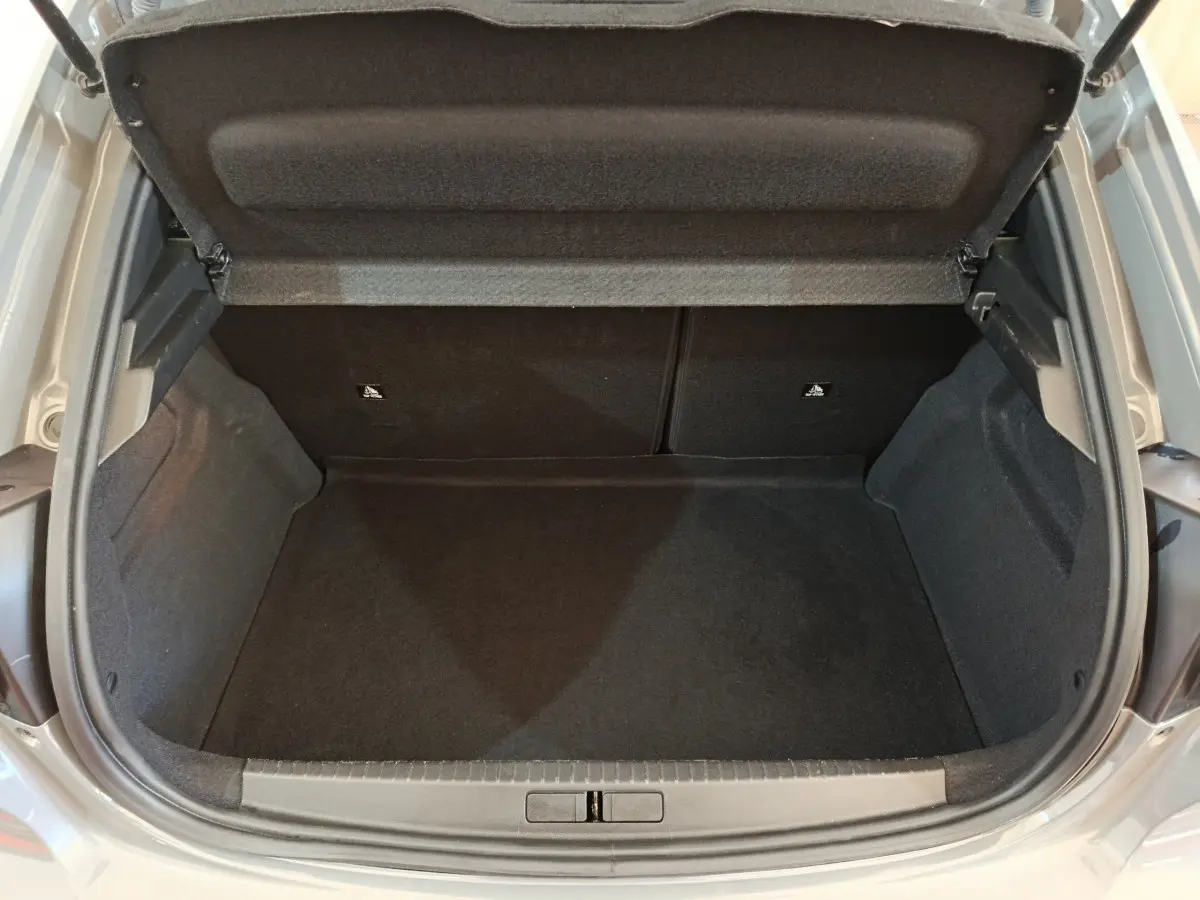 Coffre ouvert d'une Peugeot 208 gris foncé, vue de dessus montrant l'espace de rangement vide et les garnitures intérieures noires.