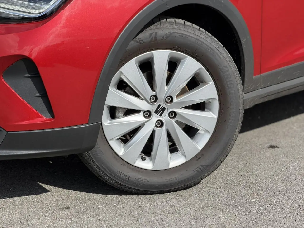 Gros plan sur la roue avant droite d'une SEAT Arona Rouge Désir avec jante alliage 16 pouces et partie du pare-chocs avant.