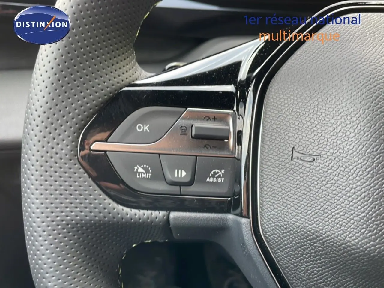 Gros plan sur le volant en cuir perforé noir de la Peugeot 308 gris Artense, avec commandes intégrées visibles.