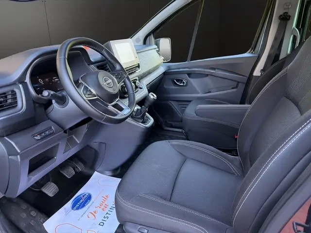 Vue intérieure côté conducteur du Nissan Primastar 2025, tableau de bord moderne avec écran tactile et volant cuir noir.