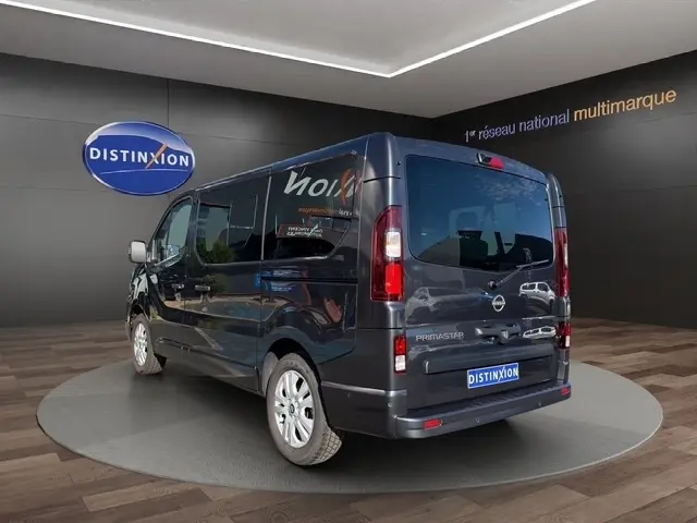 Vue 3/4 arrière droite d'un Nissan Primastar gris foncé avec vitres teintées, sur plateau en showroom Distinxion.