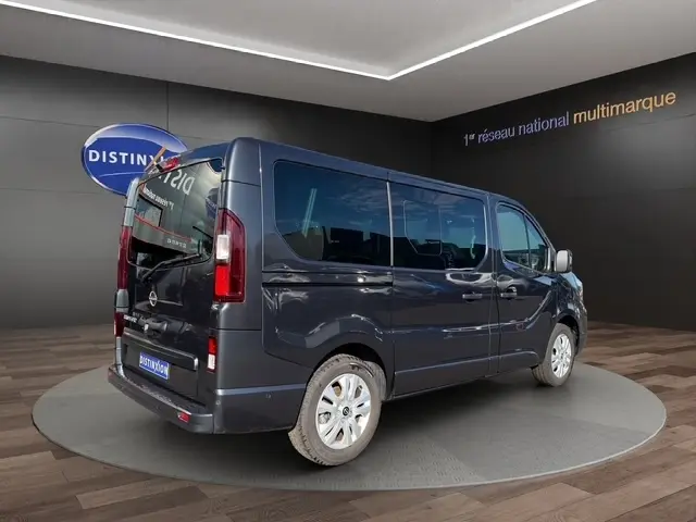 Vue 3/4 arrière droite d’un Nissan Primastar gris foncé avec vitres teintées et portes latérales, en showroom.