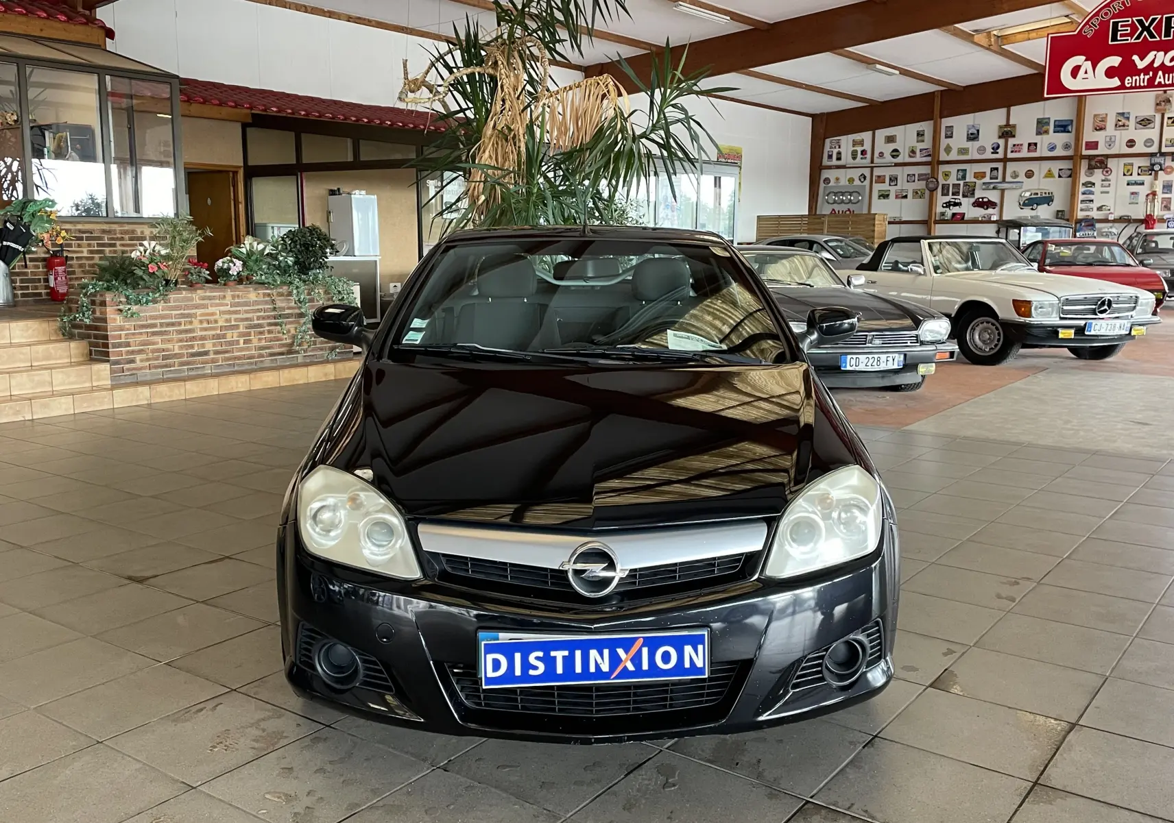 Opel Tigra Twintop noir vue de face en intérieur, avec plaque Distinxion et phares arrondis visibles.