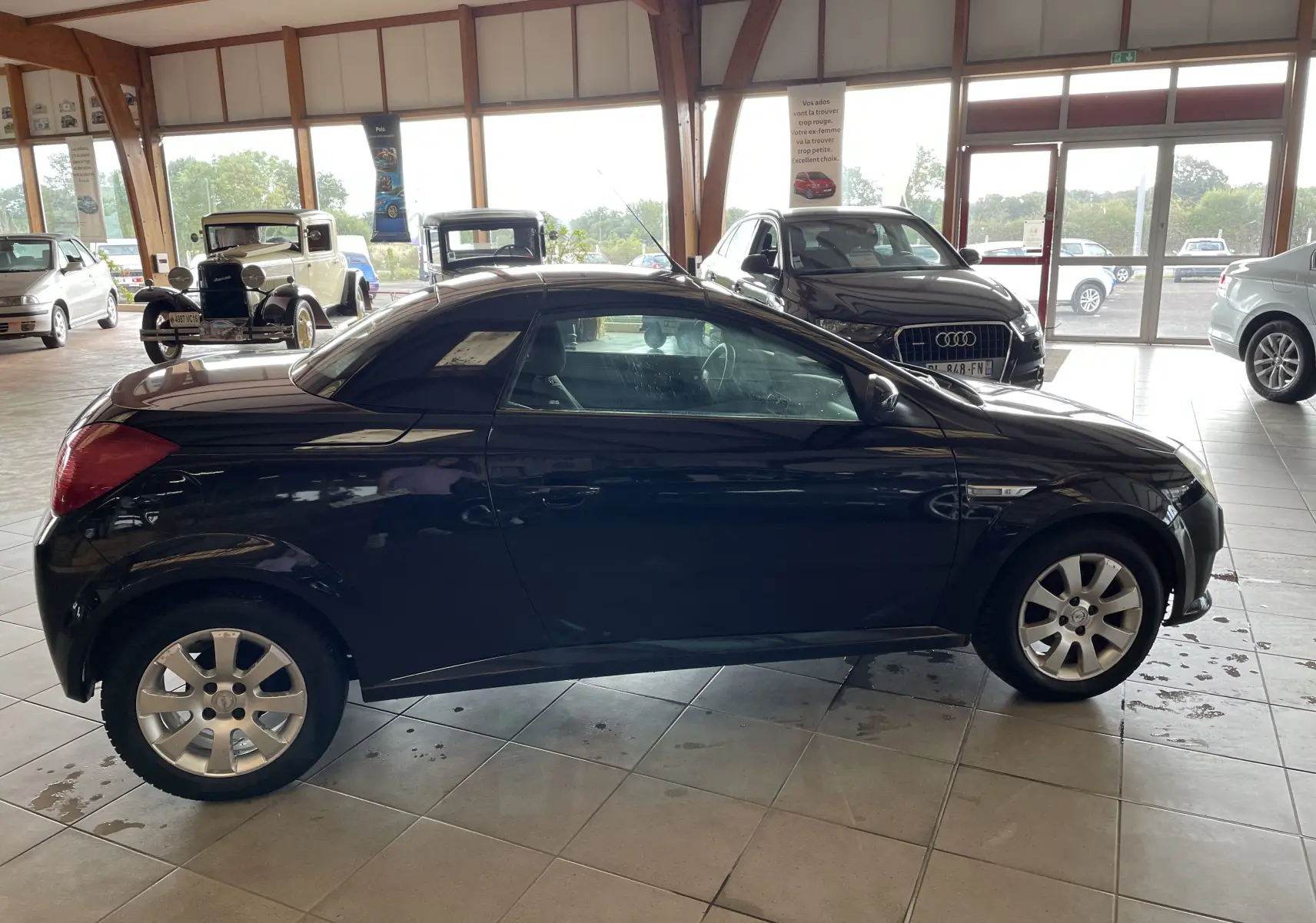 Profil côté gauche d'une Opel Tigra Twintop noire de 2006, coupé compact avec toit rigide rétractable en showroom.
