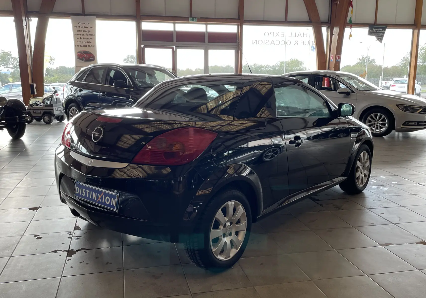 Opel Tigra Twintop noir vue 3/4 arrière droit dans un showroom, toit rigide fermé et jantes alliage visibles.