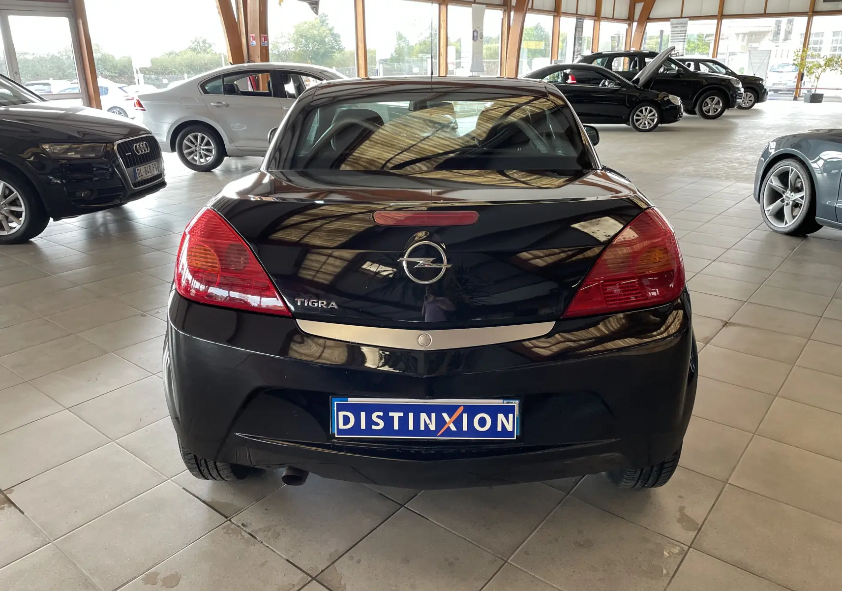 Vue arrière d'une Opel Tigra Twintop noire de 2006, avec feux arrière rouges et plaque Distinxion visible en intérieur showroom.