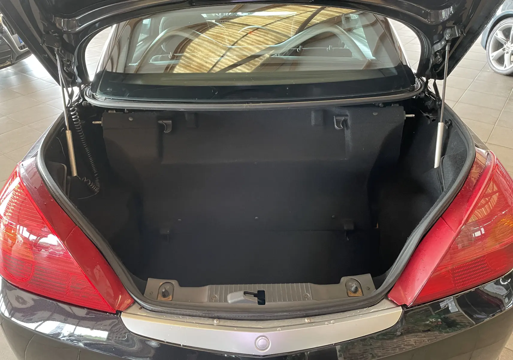 Coffre ouvert vu de l'arrière d'une Opel Tigra Twintop noire de 2006, avec feux arrière rouges visibles.