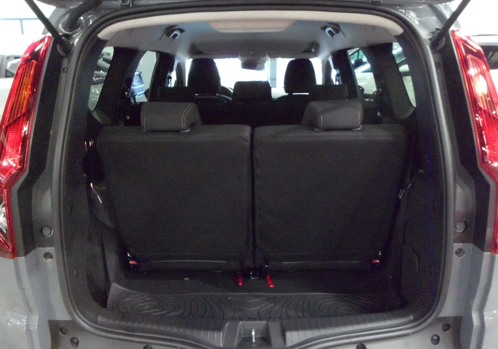 Vue arrière du coffre ouvert d'un Dacia Jogger gris urbain 2025, mettant en valeur les sièges arrière rabattus en tissu noir.