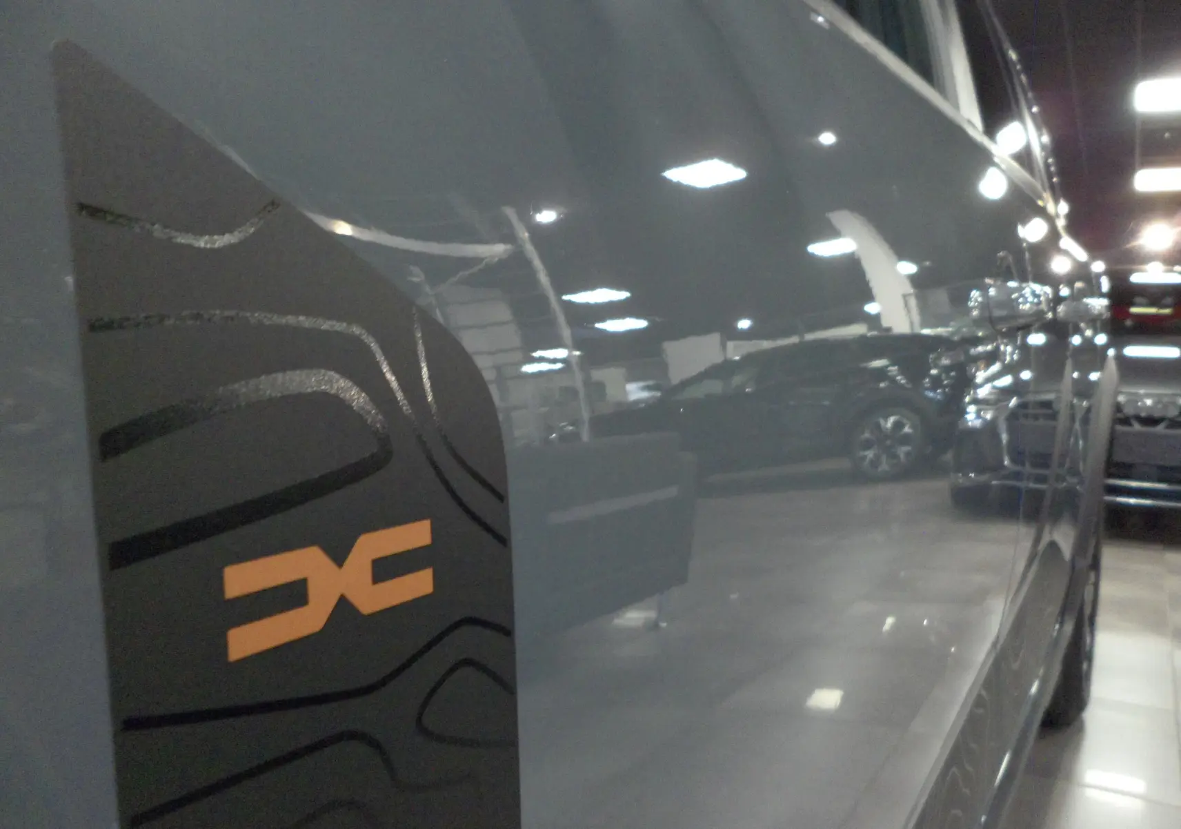 Détail du logo EXTREME orange sur la porte côté droit d'un Dacia Jogger gris urbain en intérieur showroom.