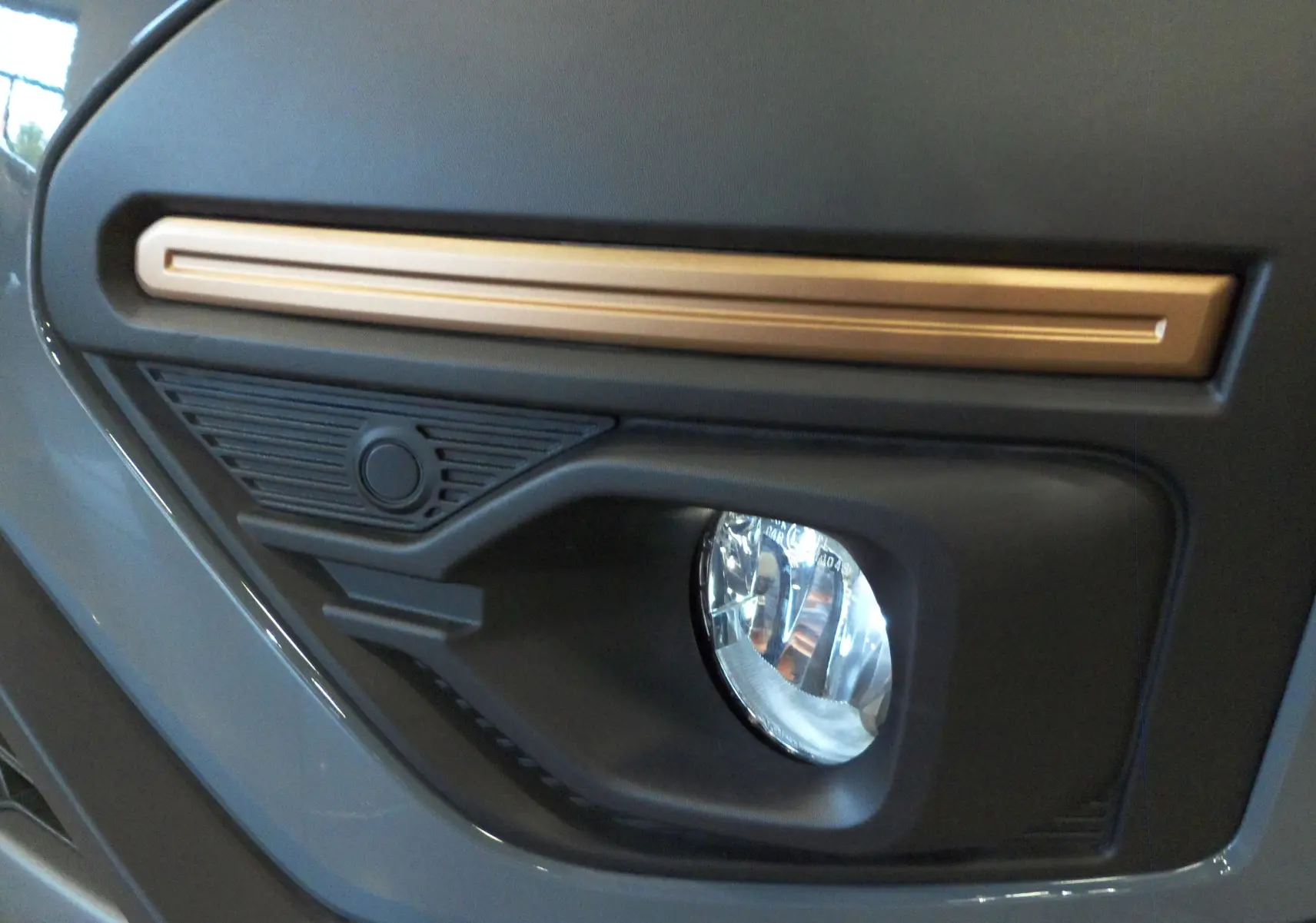 Gros plan sur le feu antibrouillard avant droit du Dacia Jogger TCe 110 Gris Urbain avec insert doré.