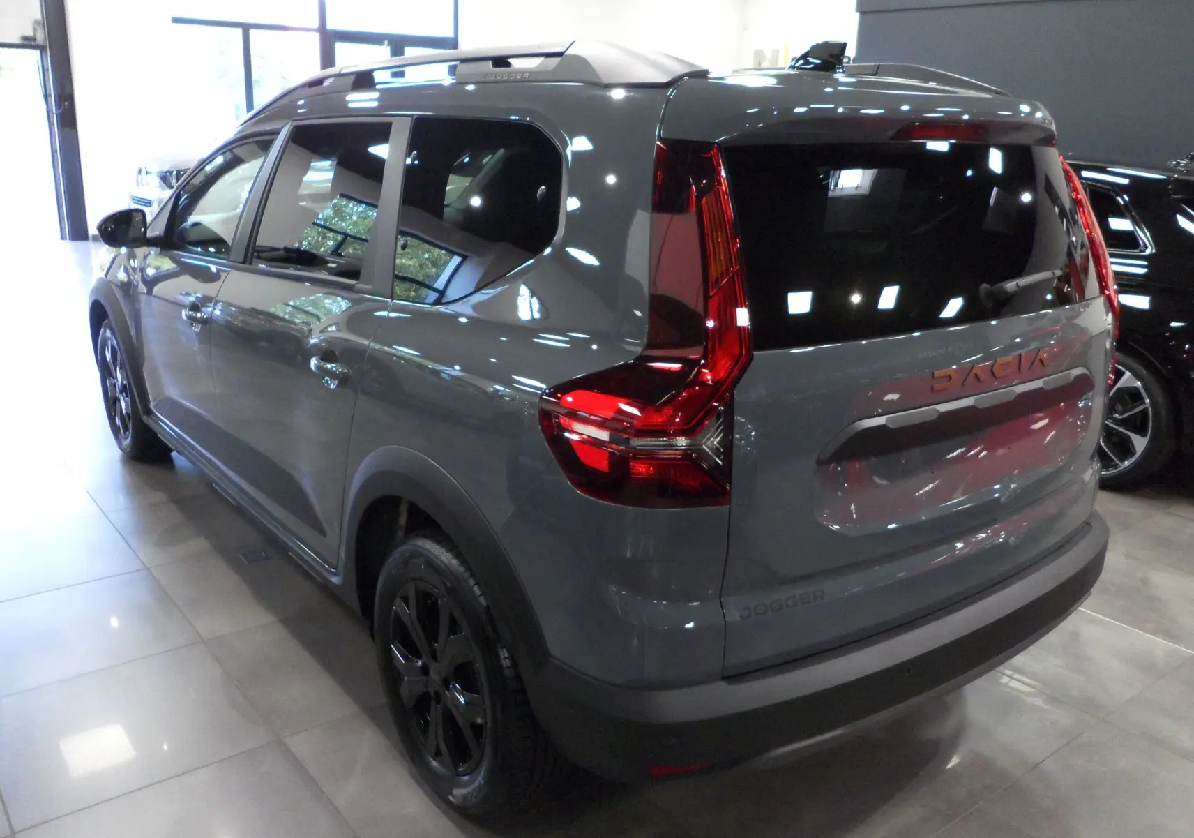 Vue 3/4 arrière gauche d'un Dacia Jogger gris urbain 2025 avec feux arrière en forme de C et jantes noires.