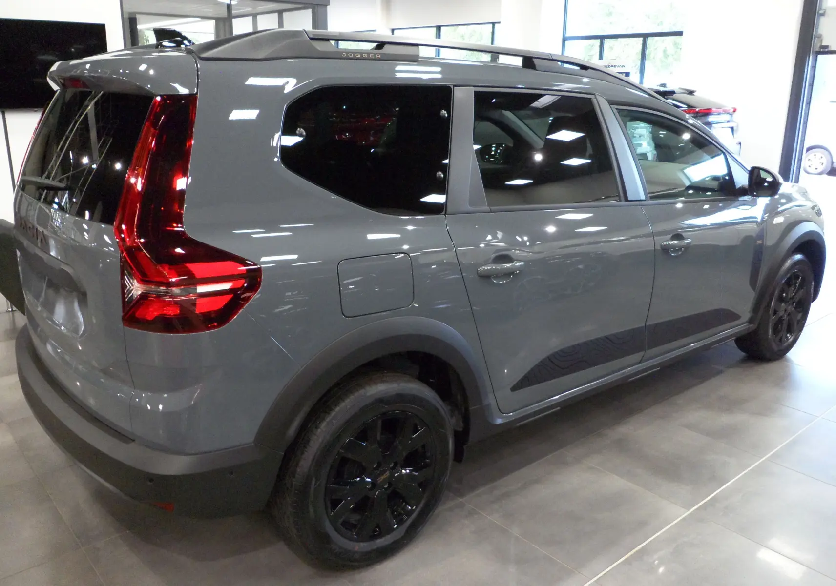 Vue 3/4 arrière droite d'un Dacia Jogger TCe 110 gris urbain avec jantes noires et vitres teintées en showroom.