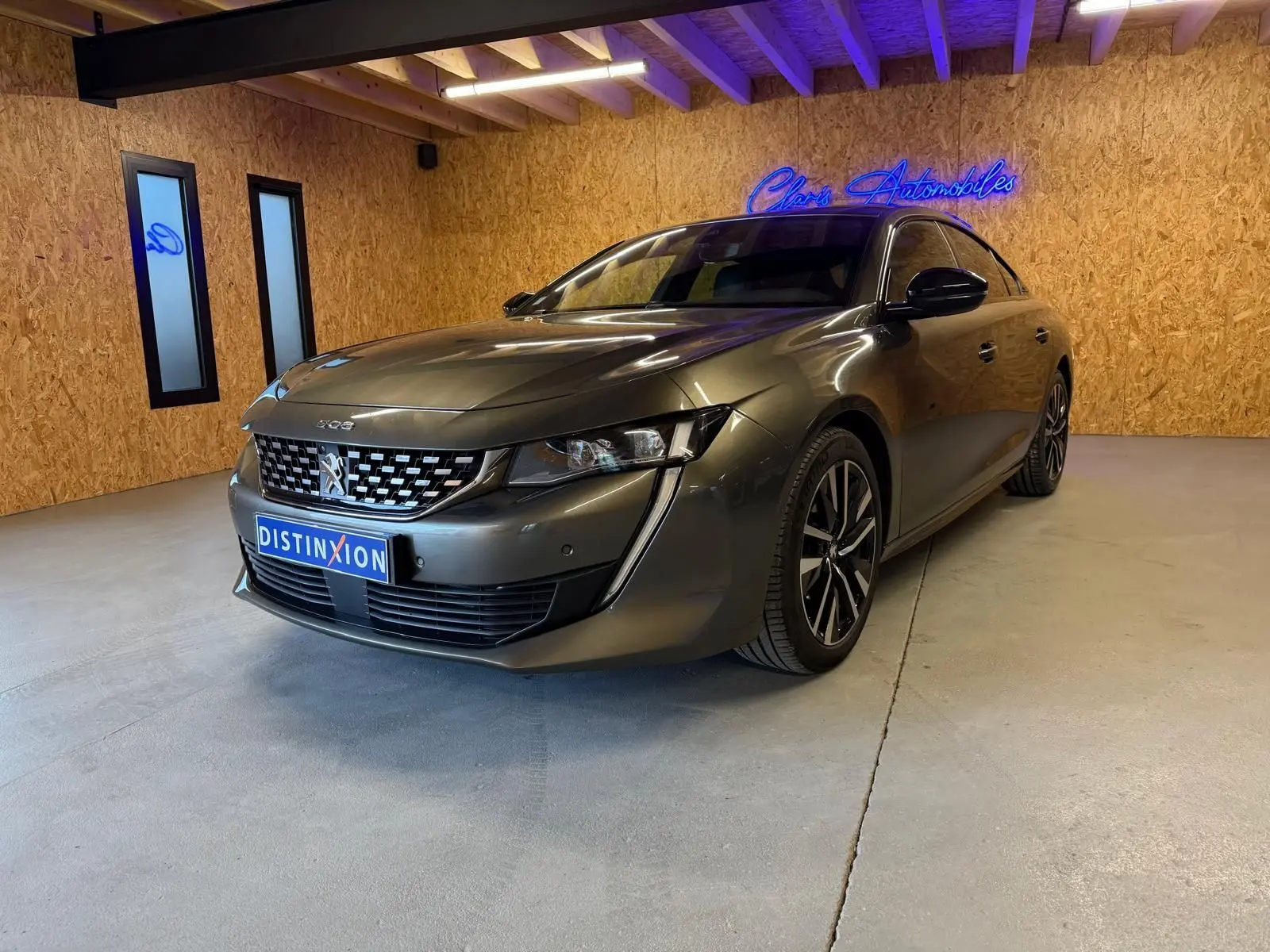 Peugeot 508 gris en 3/4 avant droit dans un intérieur avec murs en bois et éclairage néon bleu.